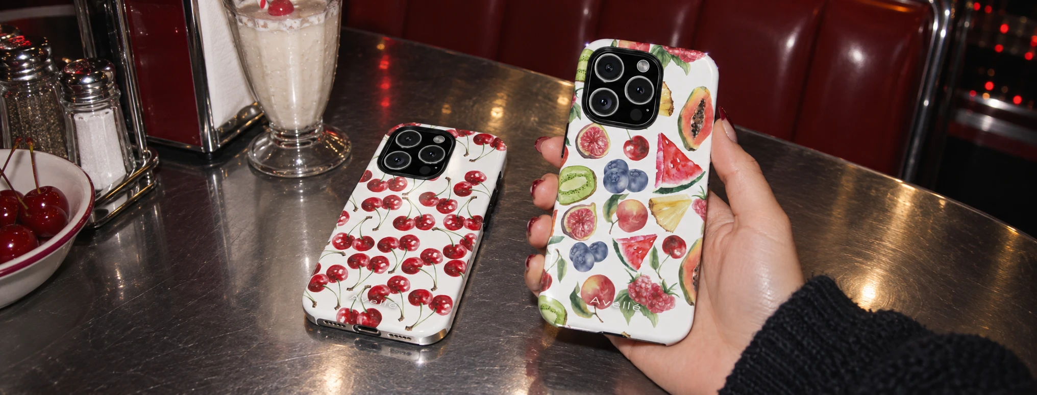 Cherry and watercolor fruit phone cases photographed in a diner